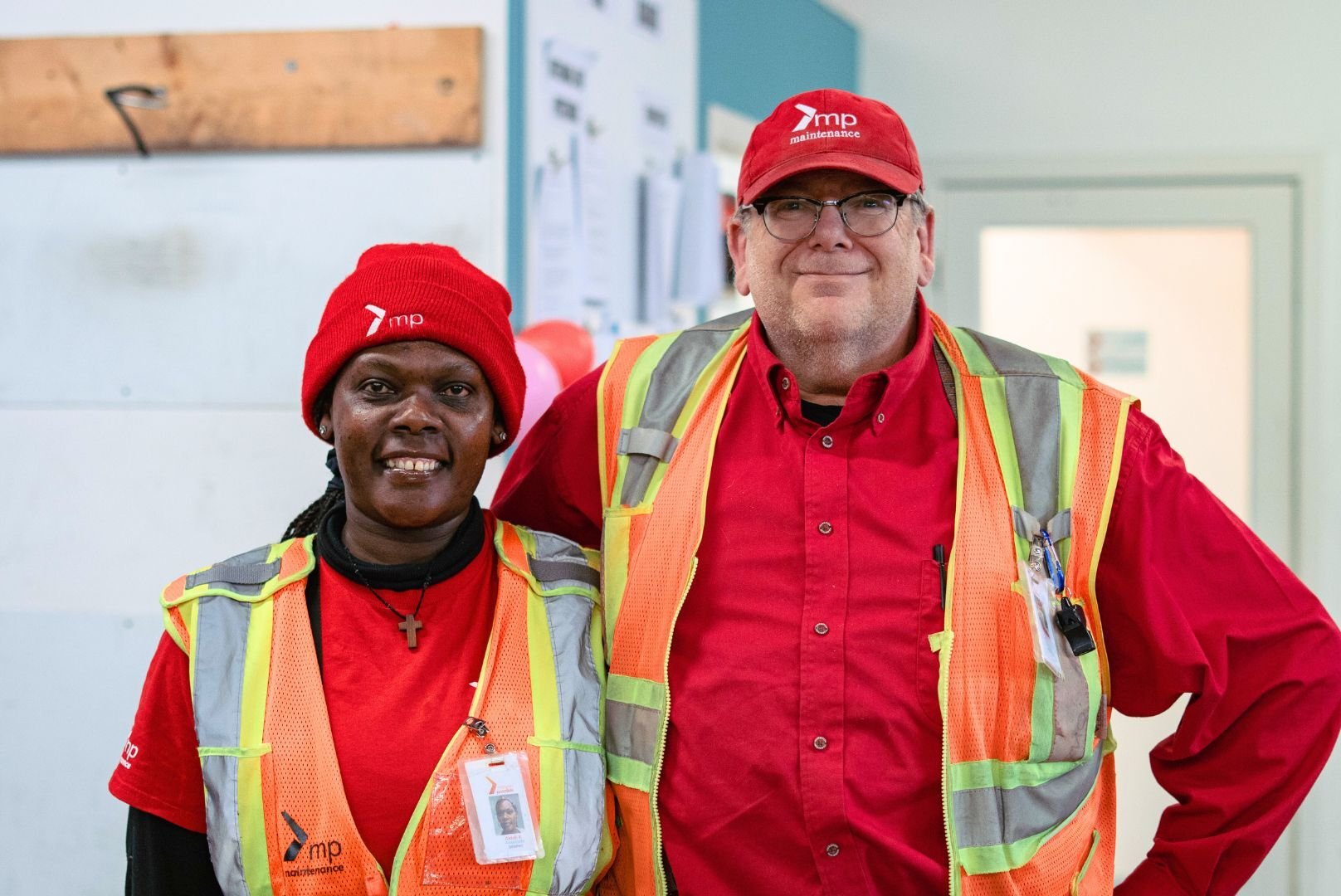 A Mission Possible associate standing next to a Mission Possible staff member. They are both wearing red MP shirt, red MP hats, and a safety vest. 